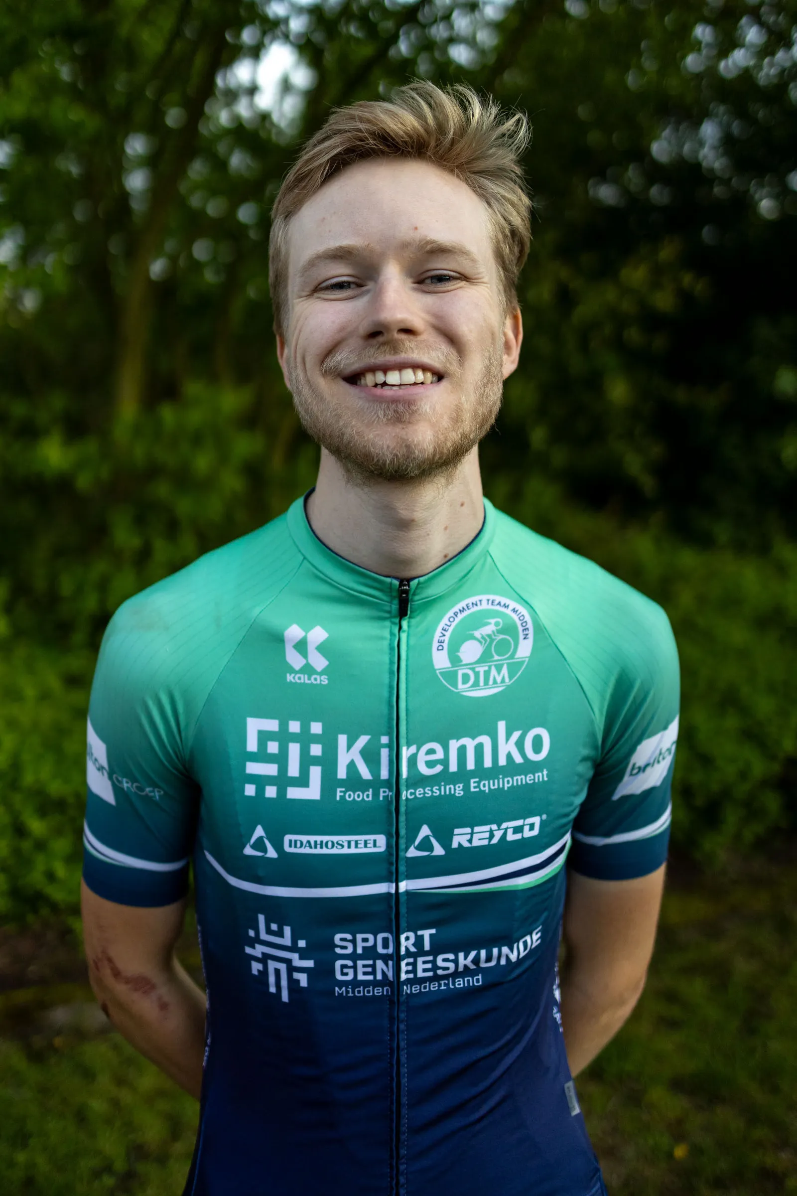 Tycho Parmentier in wielershirt, lachend, met bos op de achtergrond