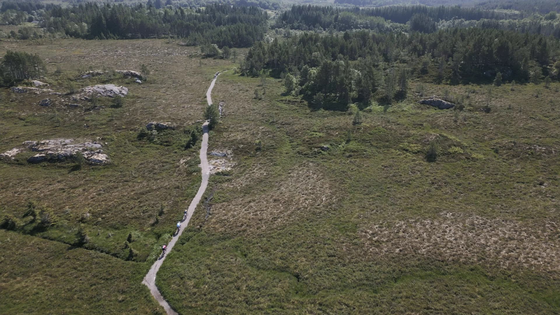 Drie renners op een grindpad door heide en rotsen, recht van boven gefilmd