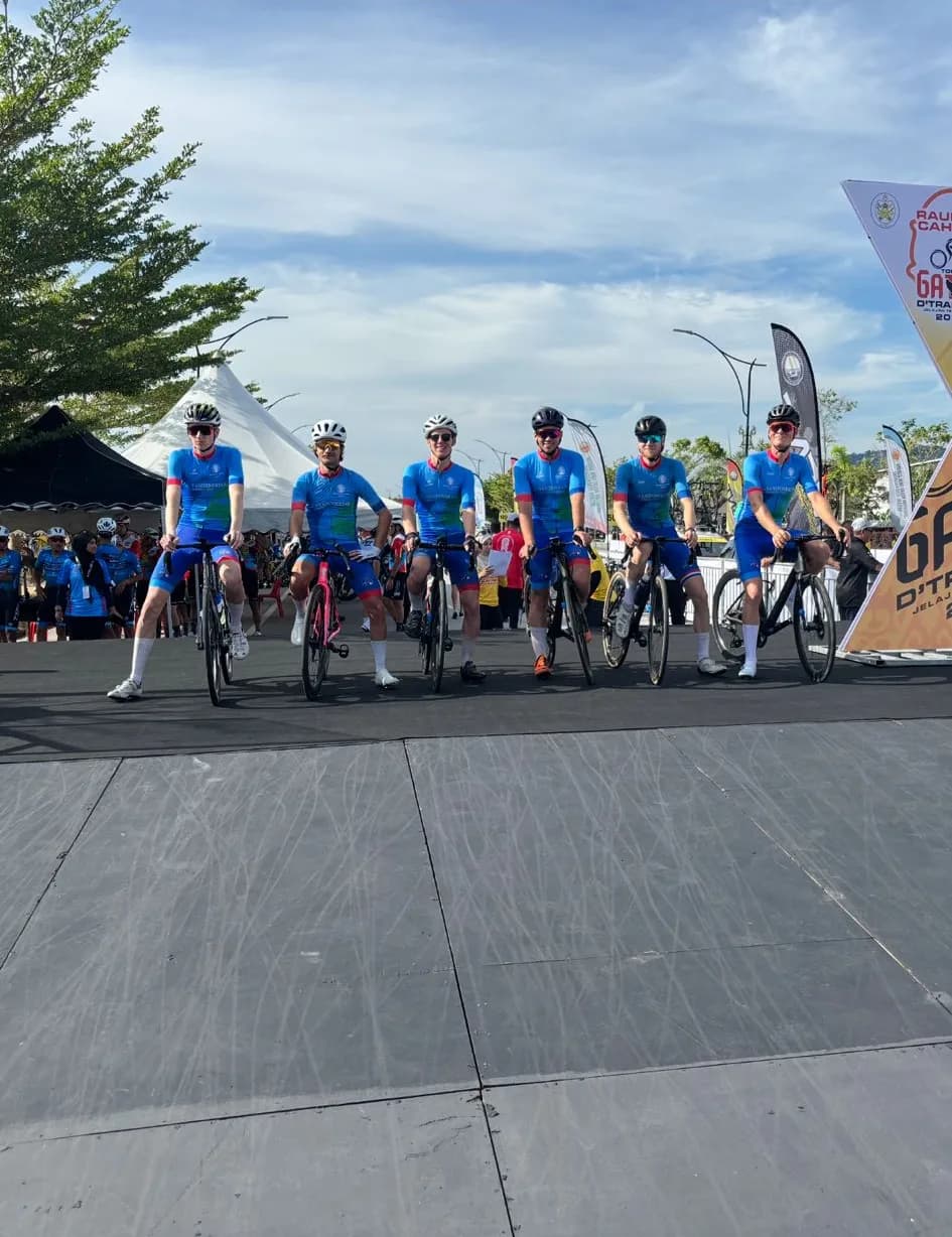 Zes renners van Team Global in teamtenue op een rij met hun fiets, bij een wedstrijd in Maleisië